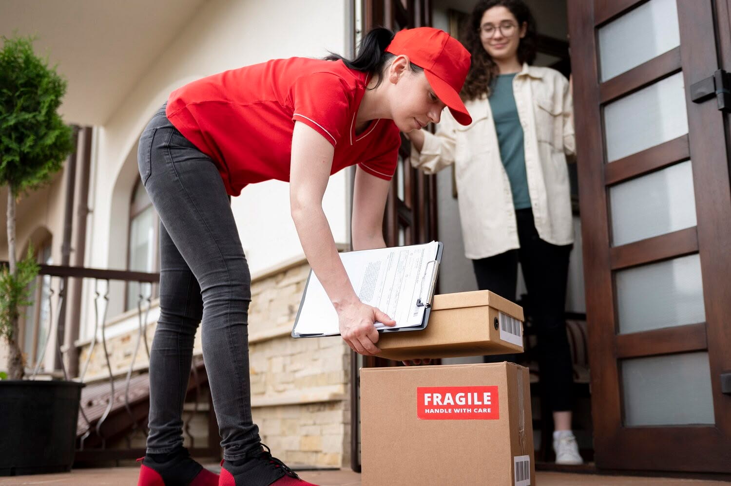 Mover in a red uniform delivering boxes to a smiling woman at her front door